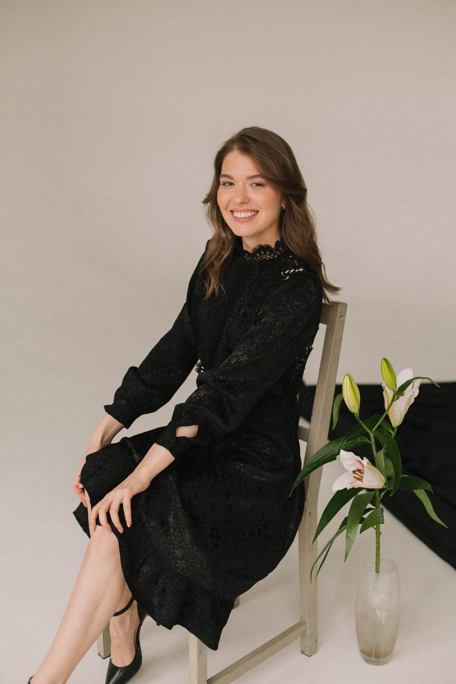 A woman seated in a black lace midi dress in a studio